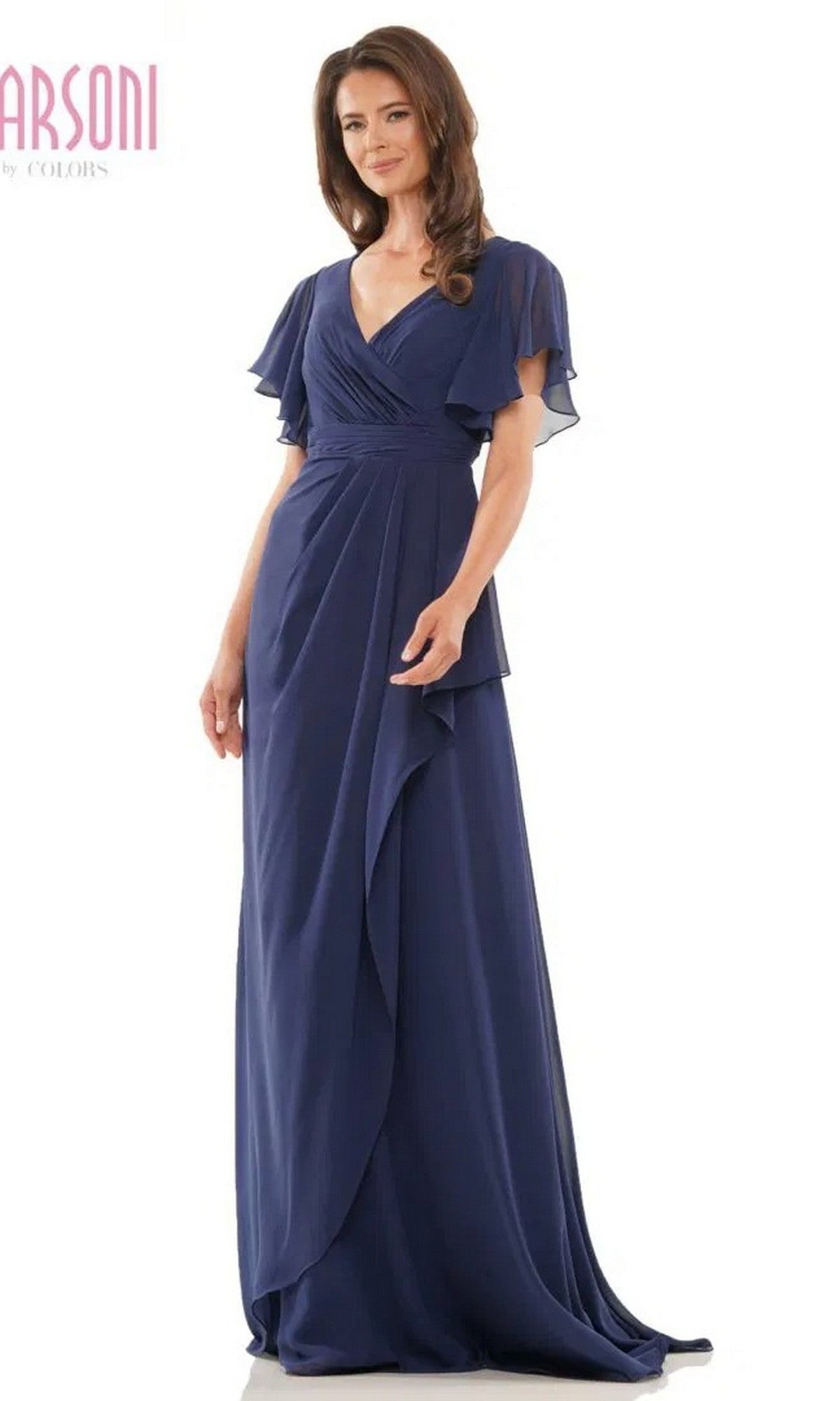 A woman stands against a white background wearing the Marsoni M320 Long Formal Dress in navy, featuring a floor-length chiffon design with flutter sleeves, an A-line skirt, and a V-neckline.